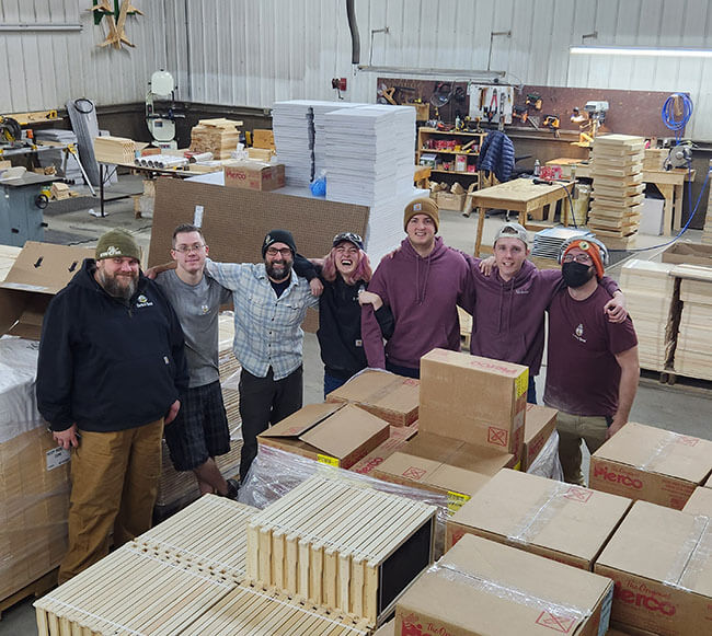 Betterbee shop crew poses and smiles among pallets of beehive frames
