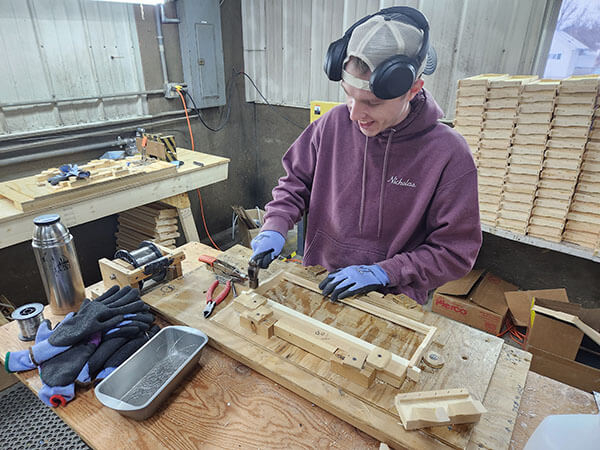 Betterbee shop crew member, Nick, wires BetterComb frames with a smile